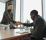 Two businessmen shaking hands in a modern office after a successful meeting or interview.
